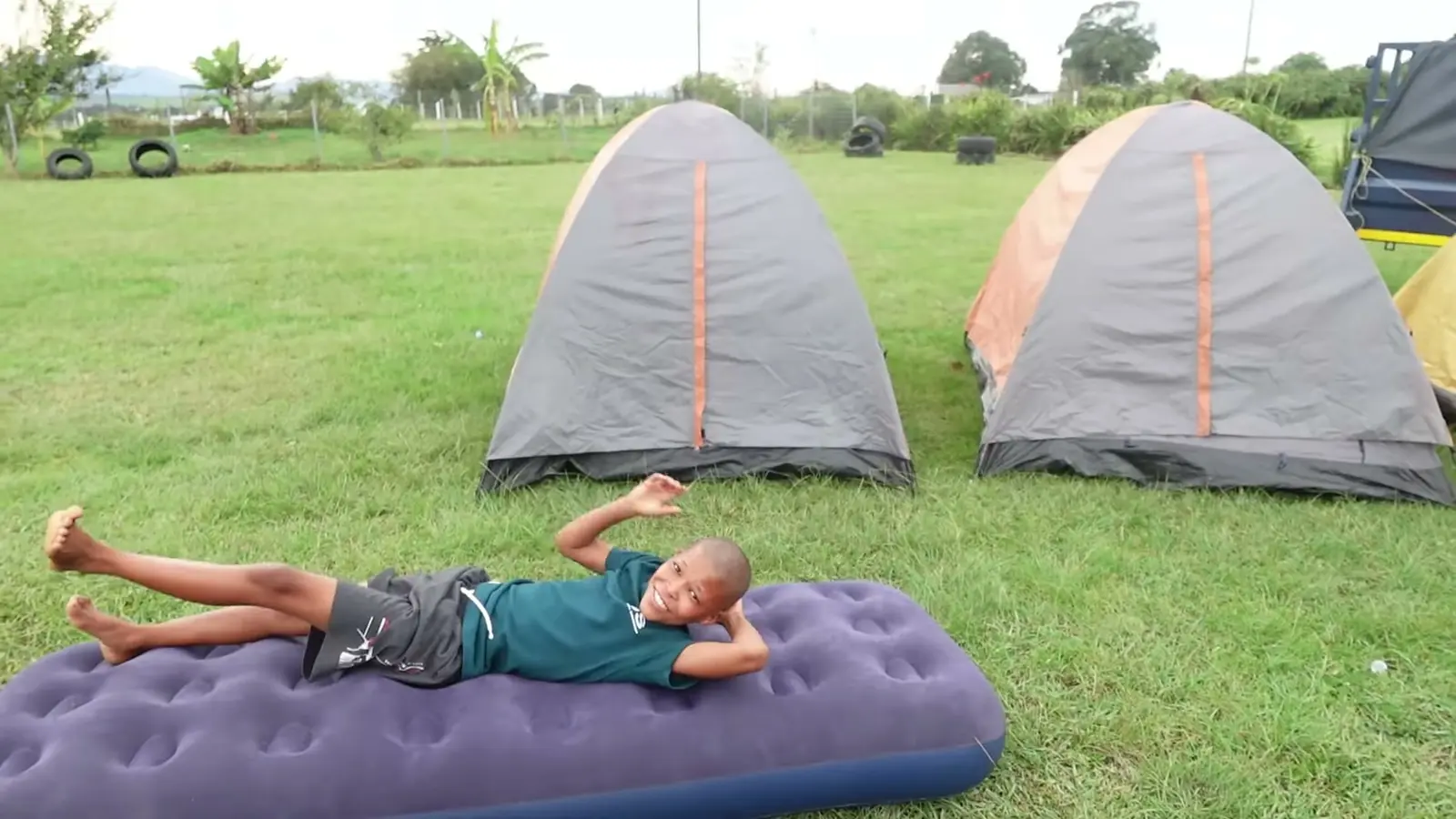 Tents on grass with a camper resting on an air mattress