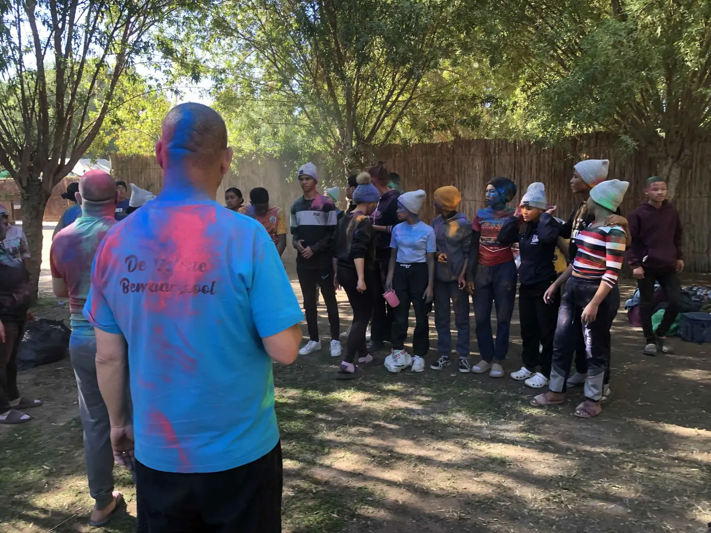 Campers covered in coloured powder stand in a circle during a game at camp