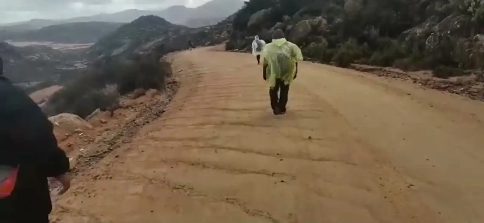 Hikers in raincoats walking along a mountain pass